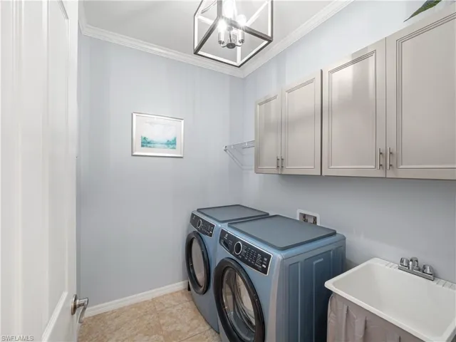 Laundry area with hanging lights, independent washer and dryer, crown molding, cabinet space, and light tile patterned flooring
