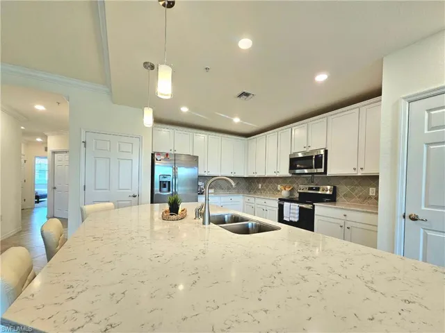 Kitchen with backsplash, a sink, light stone countertops, appliances with stainless steel finishes, and white cabinetry