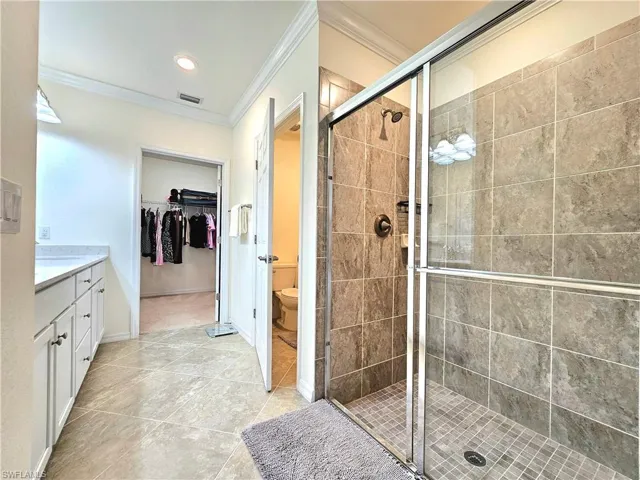 Bathroom with a shower stall, crown molding, a walk in closet, toilet, and visible vents