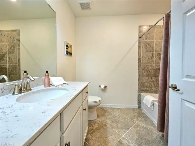 Full bath featuring tile patterned floors, vanity, toilet, visible vents, and shower / bath combination with curtain