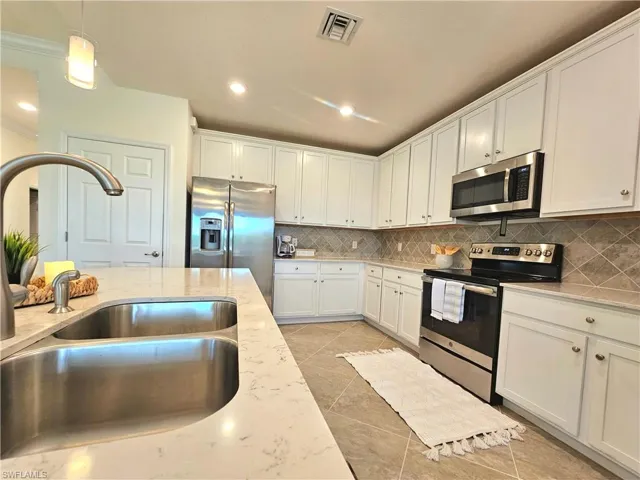 Kitchen featuring stainless steel appliances, visible vents, light tile patterned floors, a sink, and white cabinetry
