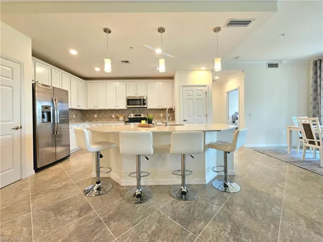 Kitchen with white cabinets, visible vents, appliances with stainless steel finishes, and decorative backsplash
