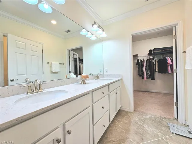 Bathroom with a spacious closet, visible vents, crown molding, and a sink