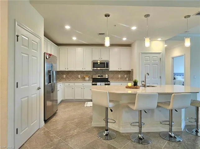 Kitchen with tasteful backsplash, white cabinetry, stainless steel appliances, and visible vents