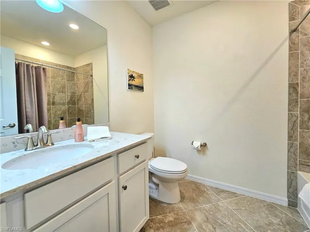 Bathroom featuring visible vents, toilet, vanity, baseboards, and tiled shower