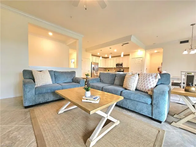 Living room with ceiling fan with notable chandelier, light tile patterned floors, baseboards, ornamental molding, and visible vents