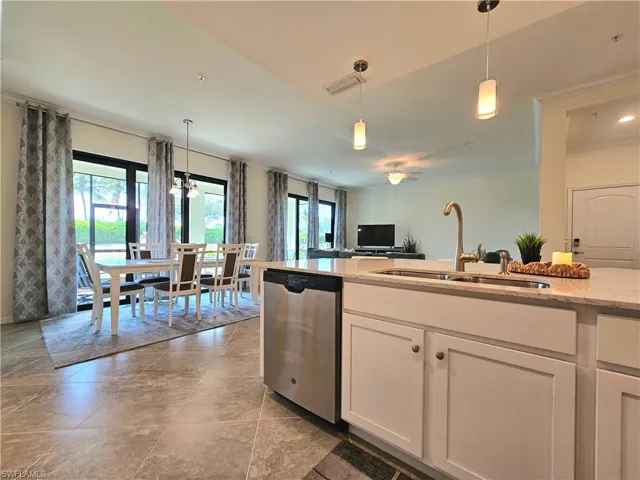 Kitchen featuring stainless steel dishwasher, a sink, decorative light fixtures, light stone countertops, and visible vents
