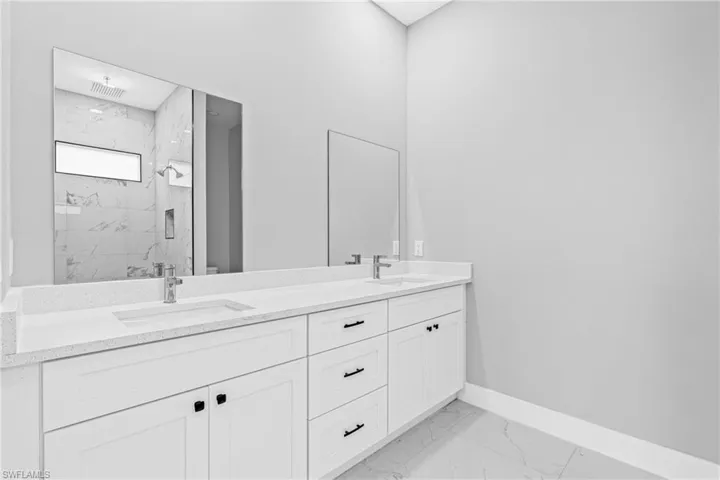 Bathroom with light marble finish flooring, double vanity, and a marble finish shower