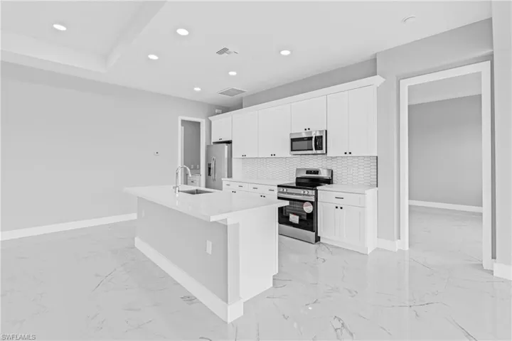 Kitchen with appliances with stainless steel finishes, a center island with sink, white cabinetry, light marble finish floors, and recessed lighting