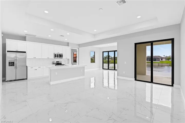 Kitchen with light marble finish floors, a raised ceiling, appliances with stainless steel finishes, open floor plan, and tasteful backsplash