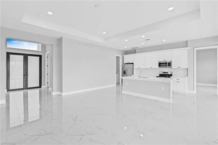 Kitchen with a tray ceiling, light marble finish floors, white cabinets, open floor plan, and recessed lighting