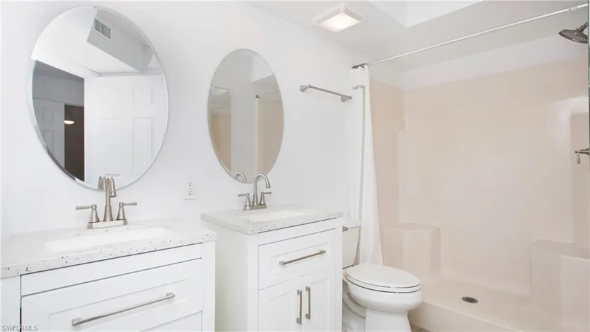 Primary bathroom with a shower stall, two vanities, and toilet