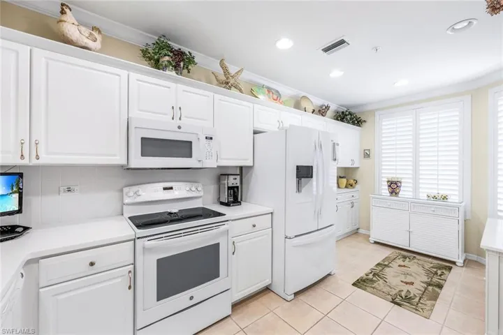 Kitchen featuring tasteful backsplash, white appliances, white cabinets, and light tile patterned floors