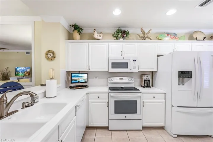 Kitchen featuring white appliances, sink, white cabinetry, and light tile patterned floors
