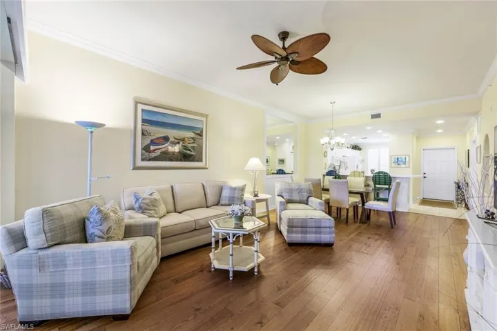 Living room featuring ceiling fan with notable chandelier, ornamental molding, and hardwood / wood-style flooring