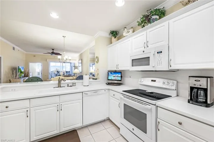 Kitchen featuring white appliances, ceiling fan with notable chandelier, light tile patterned flooring, white cabinetry, and sink