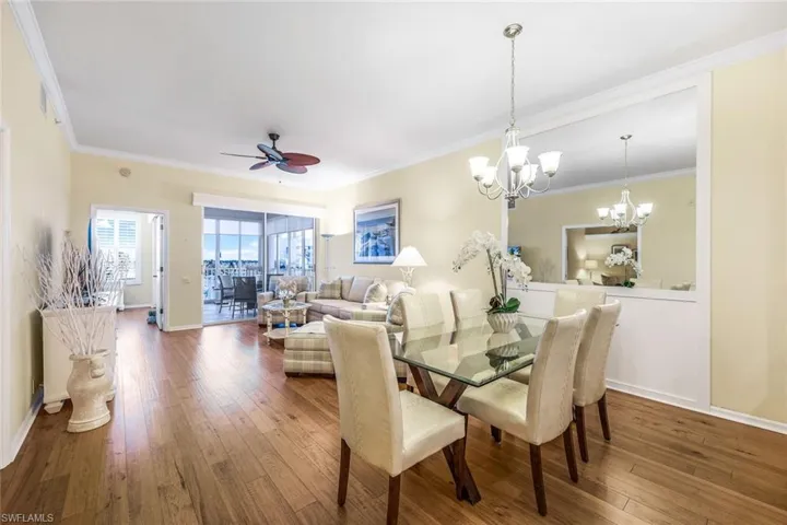 Dining room with ceiling fan with notable chandelier, hardwood / wood-style floors, and crown molding