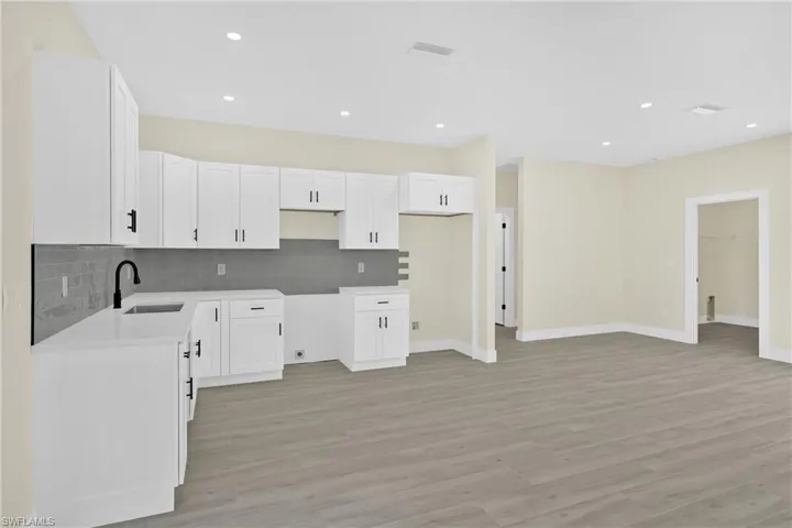 Kitchen with white cabinets, decorative backsplash, light wood-style floors, recessed lighting, and light stone counters