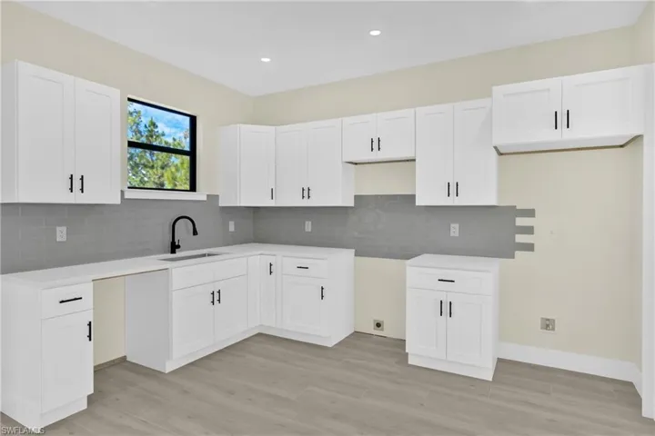 Kitchen with white cabinets, light wood-style floors, tasteful backsplash, recessed lighting, and light stone counters