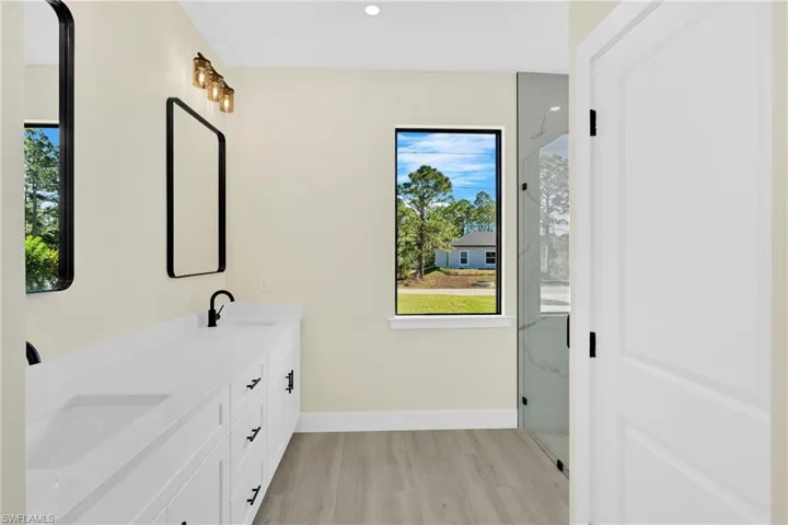 Full bathroom with double vanity, a marble finish shower, light wood-style flooring, and recessed lighting