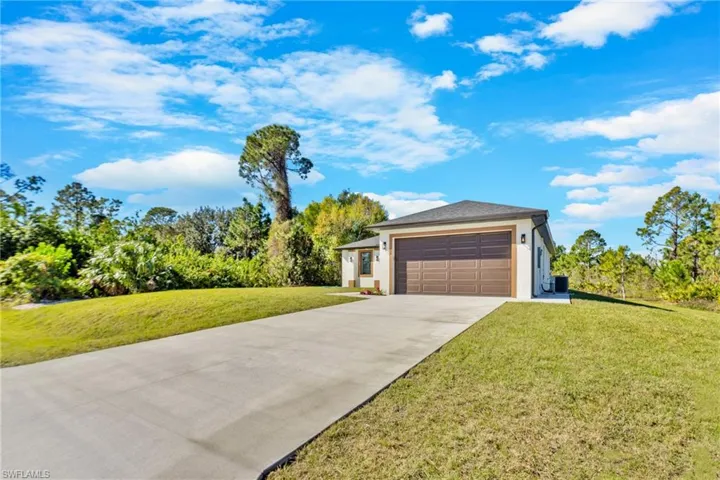 View of front of house with concrete driveway, a front lawn, stucco siding, a garage, and view of scattered trees