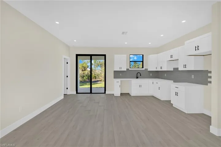 Kitchen with white cabinetry, light wood-style flooring, backsplash, light countertops, and recessed lighting