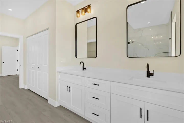 Full bathroom with double vanity, recessed lighting, a marble finish shower, and light wood-type flooring