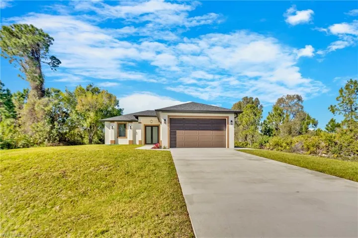 Prairie-style home featuring driveway, stucco siding, a front yard, and an attached garage