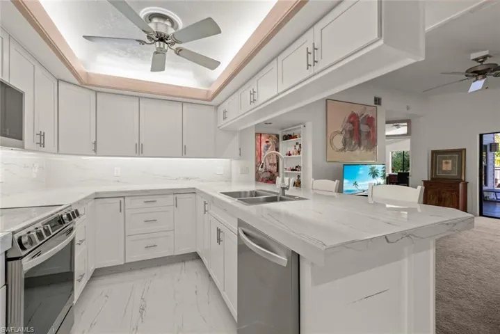 Kitchen with ceiling fan, light tile counters, stainless steel appliances, white cabinetry, and a raised ceiling