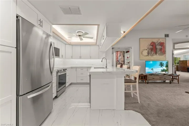 Kitchen with ceiling fan, stainless steel appliances, light tile counters, white cabinets, and a breakfast bar area