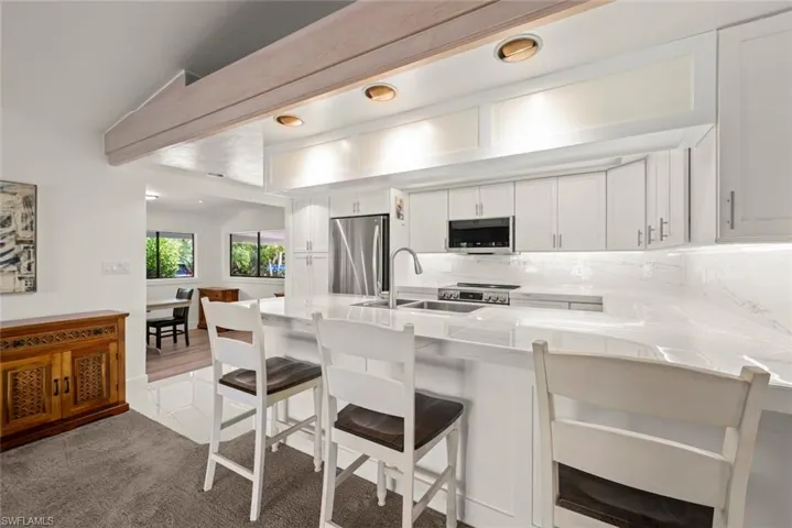 Kitchen with white cabinetry, peninsula, a kitchen bar, stainless steel appliances, and recessed lighting