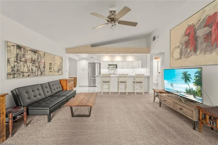 Living area with ceiling fan, light colored carpet, and vaulted ceiling