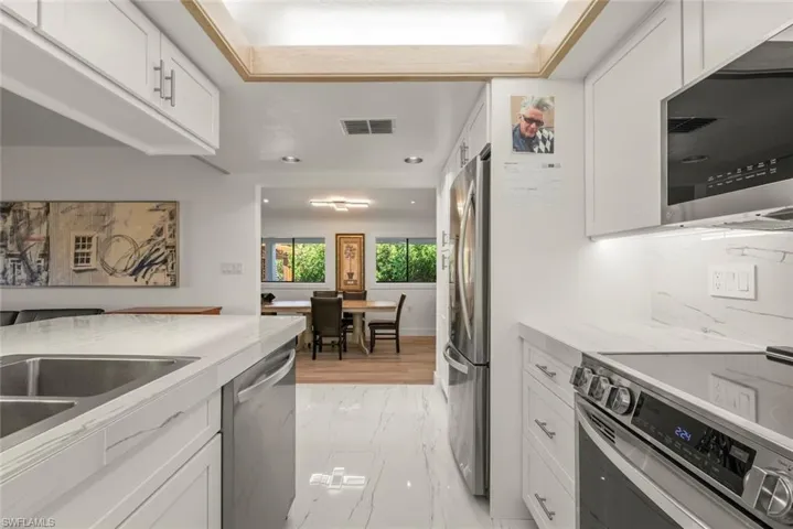 Kitchen featuring stainless steel appliances, white cabinetry, light tile countertops, light marble finish flooring, and recessed lighting
