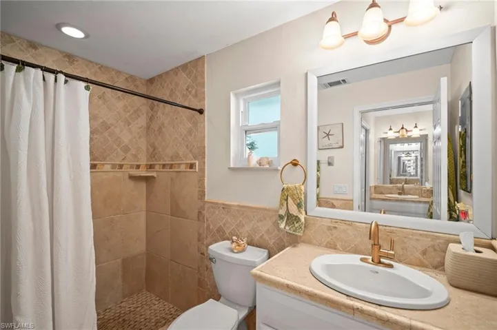 Full bath with vanity, a tile shower, tile walls, and a wainscoted wall