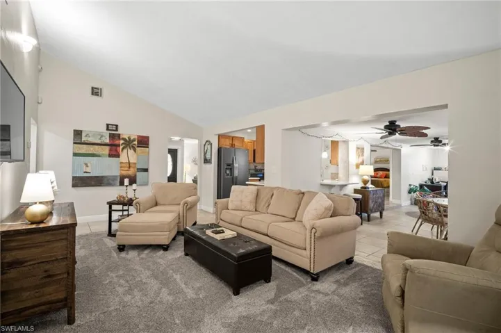 Living area featuring ceiling fan, light tile patterned flooring, light carpet, and high vaulted ceiling