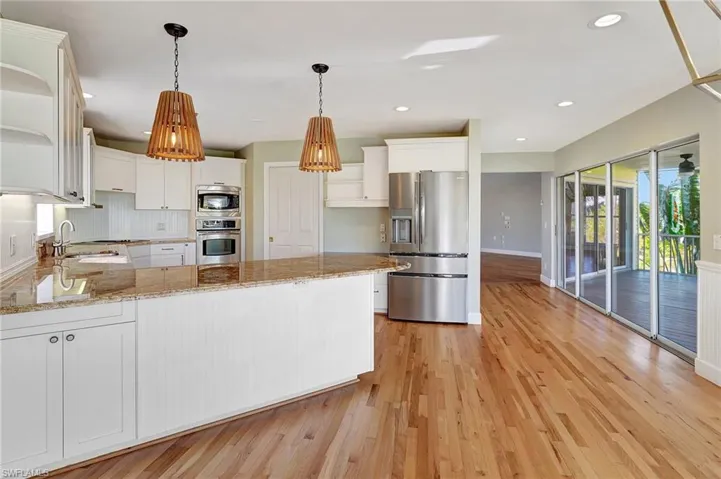Kitchen featuring appliances with stainless steel finishes, light wood-type flooring, light stone counters, sink, and white cabinetry