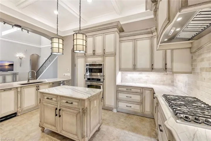 Kitchen featuring custom exhaust hood, appliances with stainless steel finishes, hanging light fixtures, a kitchen island, and sink
