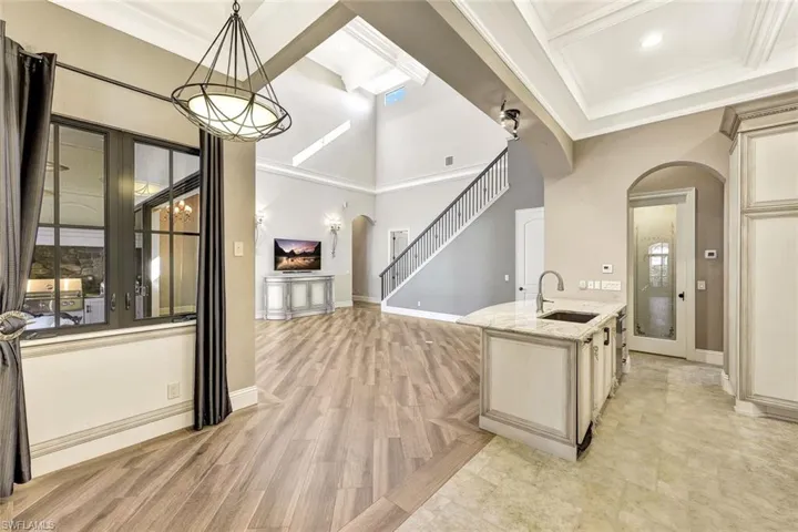 Kitchen with a towering ceiling, crown molding, pendant lighting, light stone counters, and sink