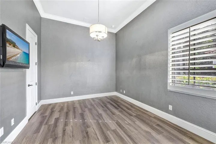 Spare room with an inviting chandelier, crown molding, and wood-type flooring