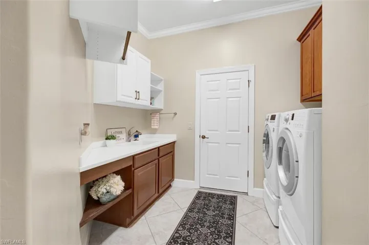 Washroom with ornamental molding, a sink, cabinet space, light tile patterned floors, and washing machine and clothes dryer
