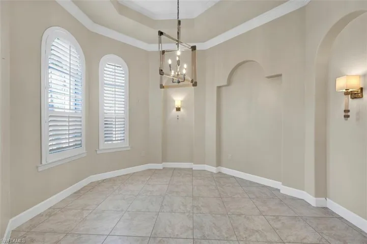 Unfurnished room featuring baseboards, ornamental molding, an inviting chandelier, arched walkways, and a raised ceiling