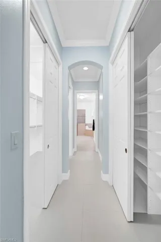 Corridor featuring light tile patterned floors, baseboards, arched walkways, and ornamental molding