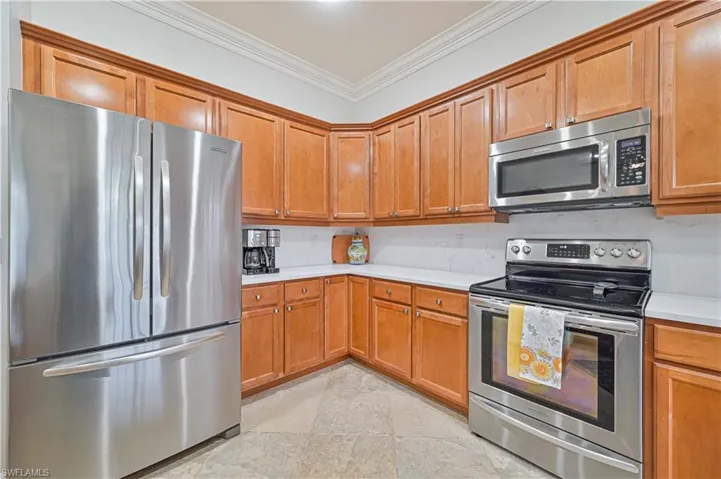Kitchen featuring stainless steel appliances, light stone finish floors, crown molding, and wood finish cabinetry