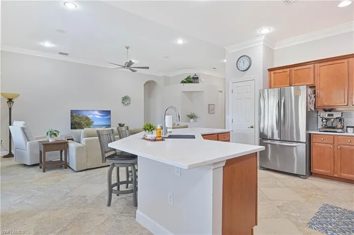 Kitchen featuring crown molding, wood finish cabinetry, freestanding refrigerator, open floor plan, and an island with sink