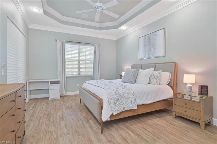 Bedroom with light wood-type flooring, crown molding, ceiling fan, and a raised ceiling