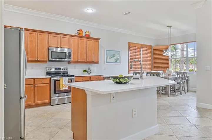 Kitchen with stainless steel appliances, an island with sink, crown molding, wood finish cabinetry, and decorative light fixtures