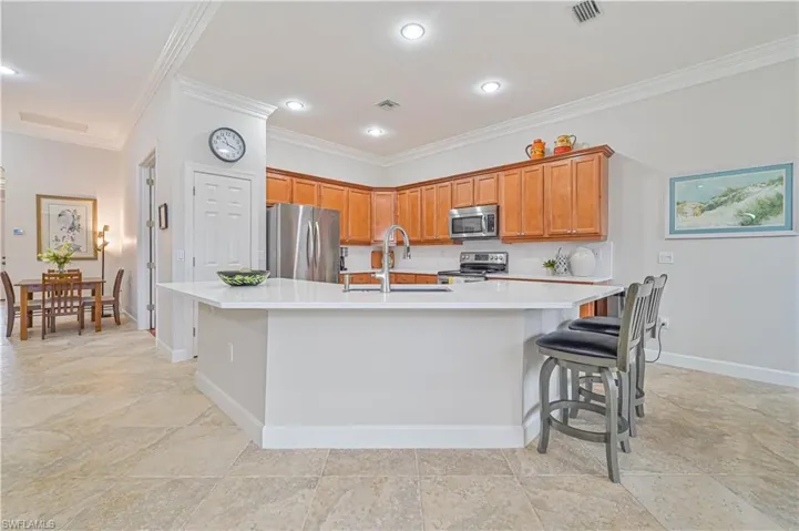 Kitchen with stainless steel appliances, a large island with sink, a breakfast bar, wood finish cabinets, and ornamental molding