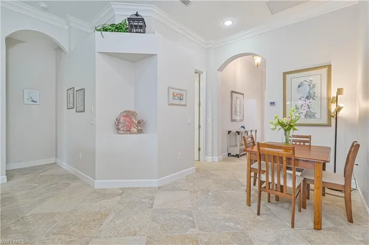 Dining room featuring arched walkways, crown molding, light stone finish flooring, and recessed lighting