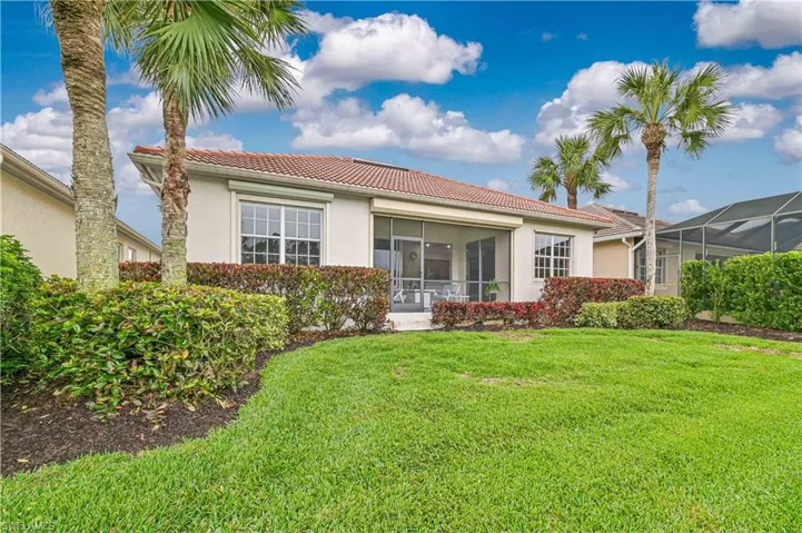 Back of property with a tile roof, stucco siding, a sunroom, and a lawn