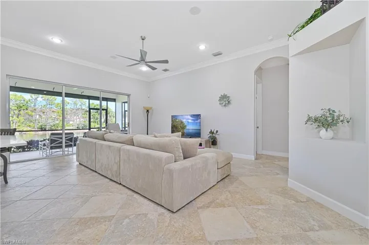 Living room with crown molding, arched walkways, a ceiling fan, stone tile floors, and recessed lighting